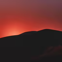 a silhouette of a hill with the sun setting behind