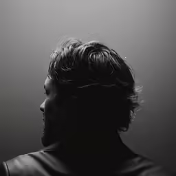 a man with his hair pulled back, standing next to a wall