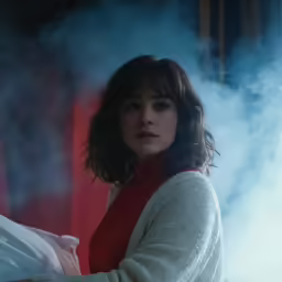 a woman standing in a dark room with white smoke behind her
