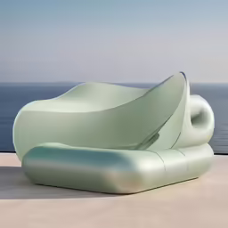 a green sculpture of a leaf on the sand near a body of water