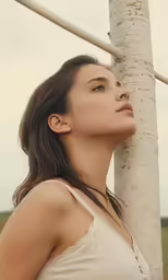the young woman poses next to a tall tree
