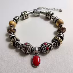 there is an interesting bracelet made out of beads and red glass beads,a bracelet on white background with charms and stones