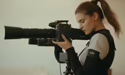 a young woman is holding a camera and wearing a ponytail while she holds it on a tripod