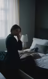 a woman in dark room with her head down next to bed