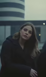 a woman is looking into the distance and in the background is a building