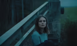 a woman sitting on a rail next to a bridge