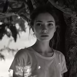 a woman is posing under a tree in the daytime