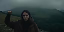 a woman in a coat raises her fist as she walks in the rain