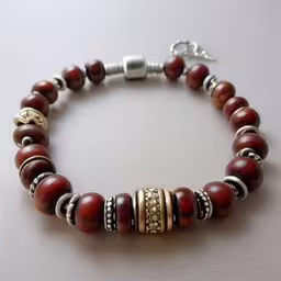 a bracelet with a charm set on top,the red and silver beaded bracelet has gold accents