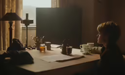 woman sitting at table looking out window in darkened room