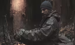 a bearded man sits in the woods looking down