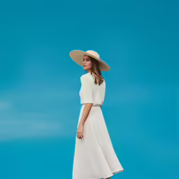 a girl standing on the sand in a white dress and straw hat
