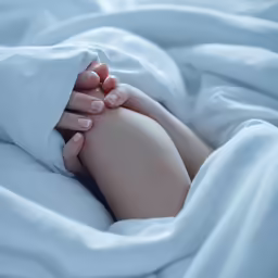 two hands touching each other on a bed with sheets