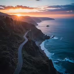 the sun sets over a winding road next to the ocean
