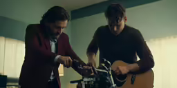 two young men perform on their guitars in a house