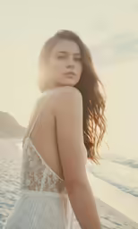 a woman is standing by the ocean at sunset