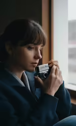 a woman is holding a camera in front of a window