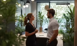 a man and woman talking while standing by some plants