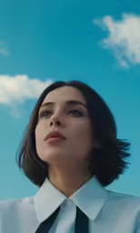 a woman with short hair, wearing a shirt and tie against the sky