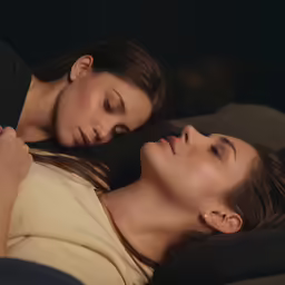 two women laying in bed together on the comforter