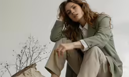 a woman with brown hair crouching in front of a tree