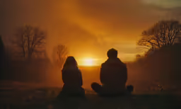two people sit near each other as the sun sets