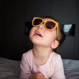 a little girl in sunglasses on top of a bed