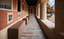 a long building with pillars, benches and art on the wall