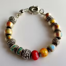 an ornate bracelet with two charms and beads,a colorful bracelet sitting on top of a table