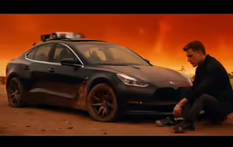 a man sits in front of his car near a bush