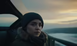a woman sitting in a car with a hat and scarf on