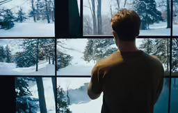a man is looking out the window at the snow