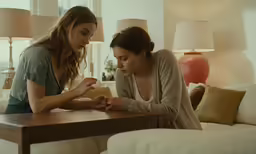 two girls are sitting at the table in a living room