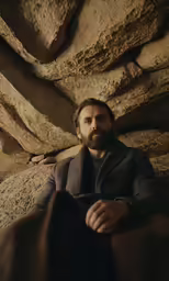 man with long beard sitting on the rocks of a rock formation