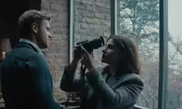 a man and woman looking out a window at a building through a binoc shades of the window
