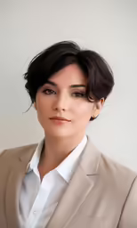 a woman with short hair, wearing a white shirt and brown blazer