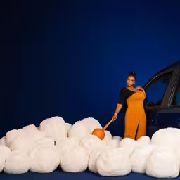 a woman is standing next to white wool balls and a car