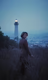 a woman standing in front of a light house near the water