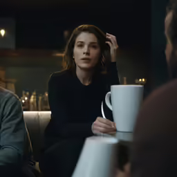 two people sit in a cafe, one holds a cup