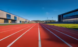 an empty track near two school buildings and grassy field