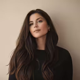 a woman with long brown hair, wearing a black blouse and looking into the distance
