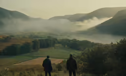 two people in coats look out over the countryside