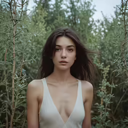 a beautiful young woman standing in front of tall trees