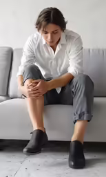 the man is sitting on a white couch and has his hands on his knees