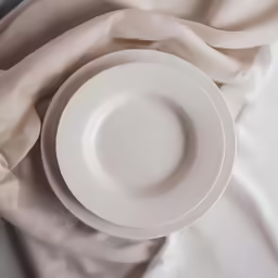 an empty plate sitting on top of a bed covered in blankets