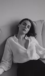 a woman is sitting on the couch wearing a shirt and black pants