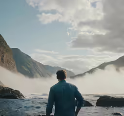 a man is standing on a rocky shore by the water