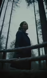 a woman in a black coat standing among a grove of trees
