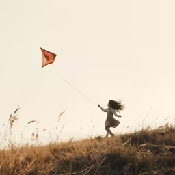 a young girl flying a kite in the grassy field
