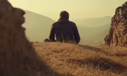 man sitting at edge of cliff overlooking mountains in hazy day